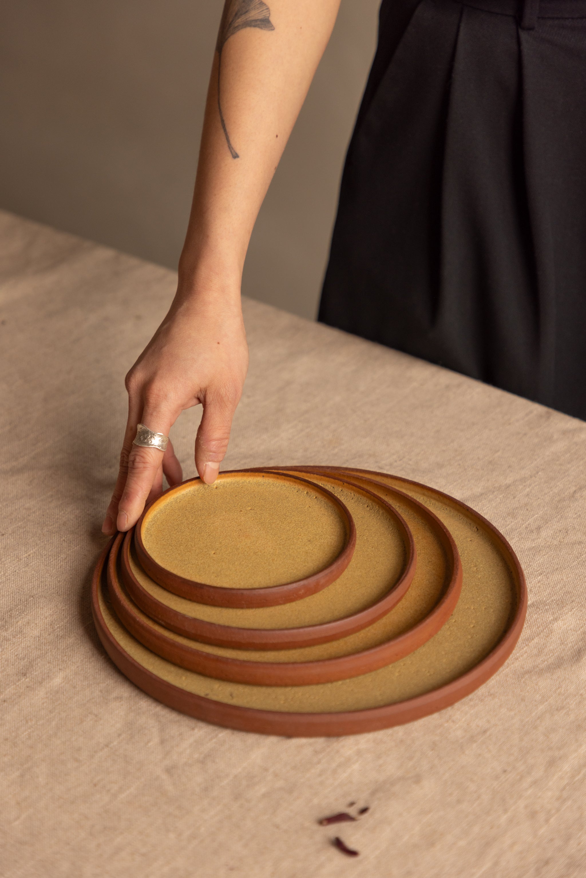 Stack of ceramic plates on a textured surface with a hand reaching for one.