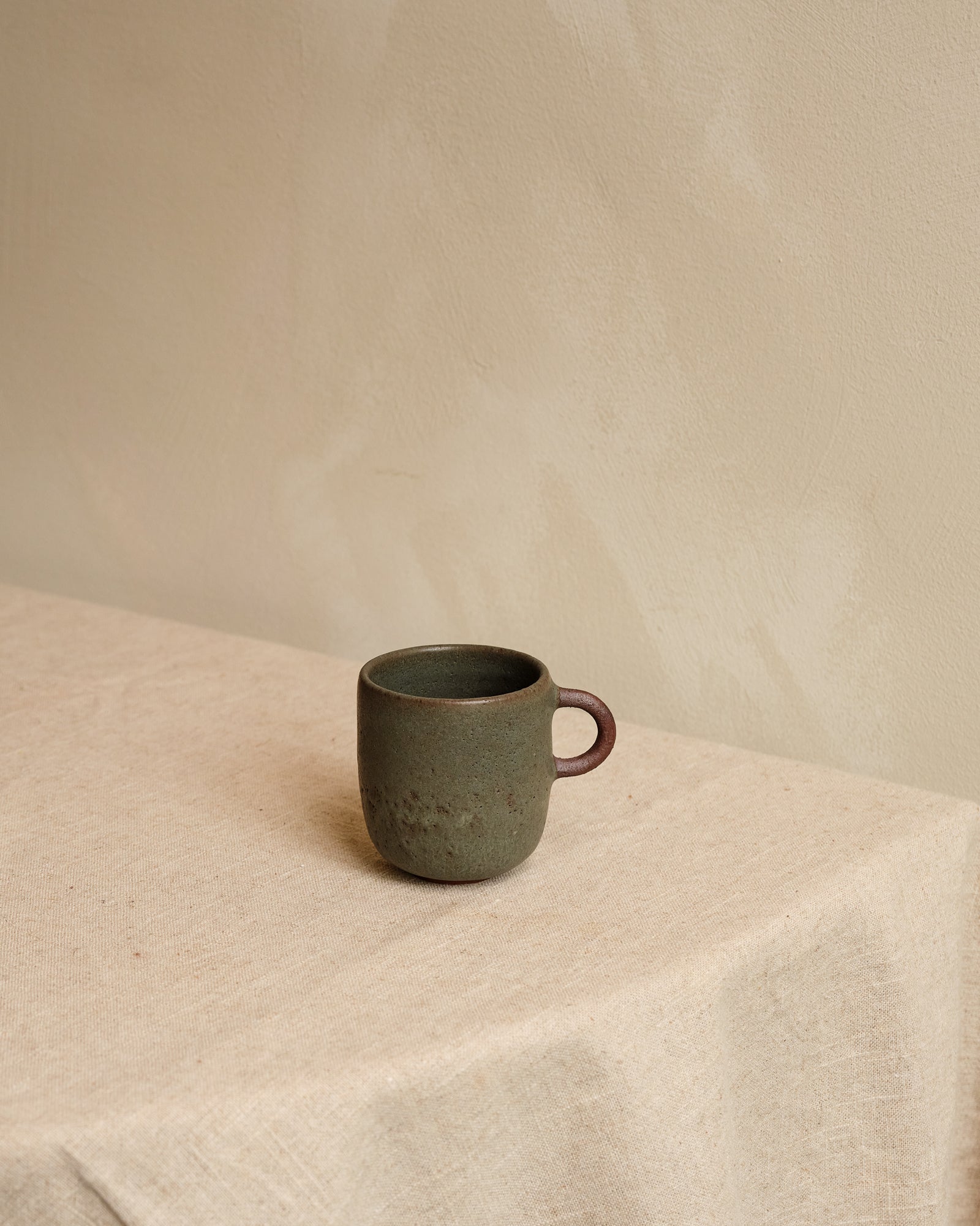 Green ceramic mug on a light fabric surface with a neutral background