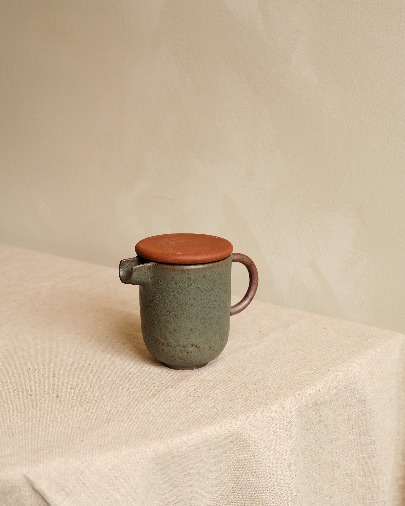 Green ceramic teapot with a brown lid on a light fabric surface.