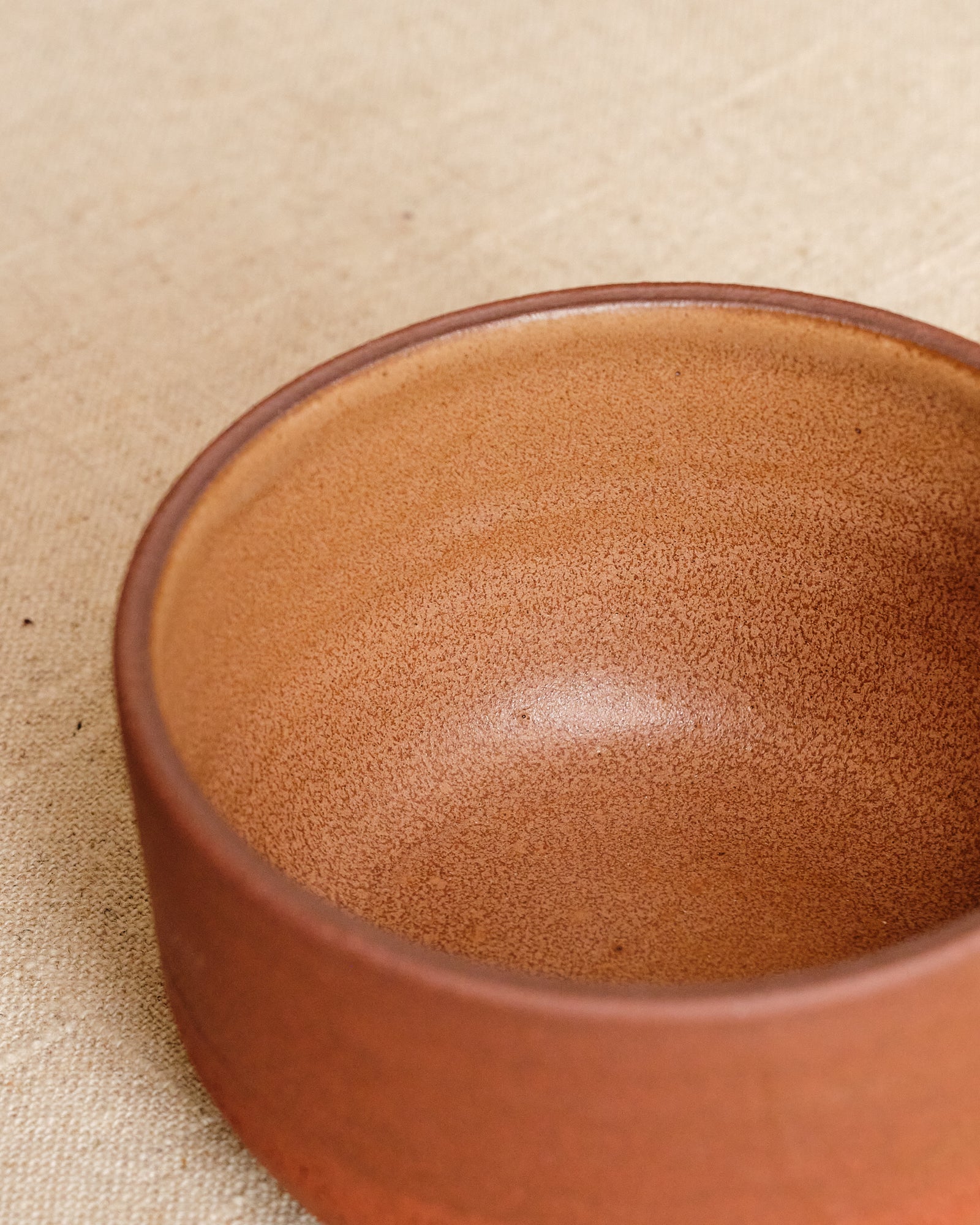 Close-up of a brown ceramic bowl on a beige fabric background