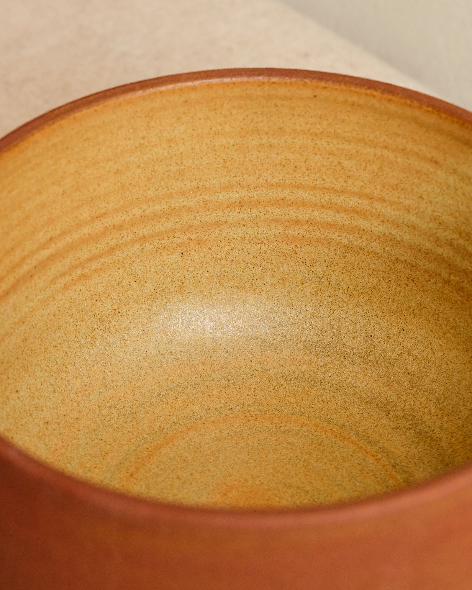 Close-up of a ceramic bowl with a brownish-orange glaze on a beige background
