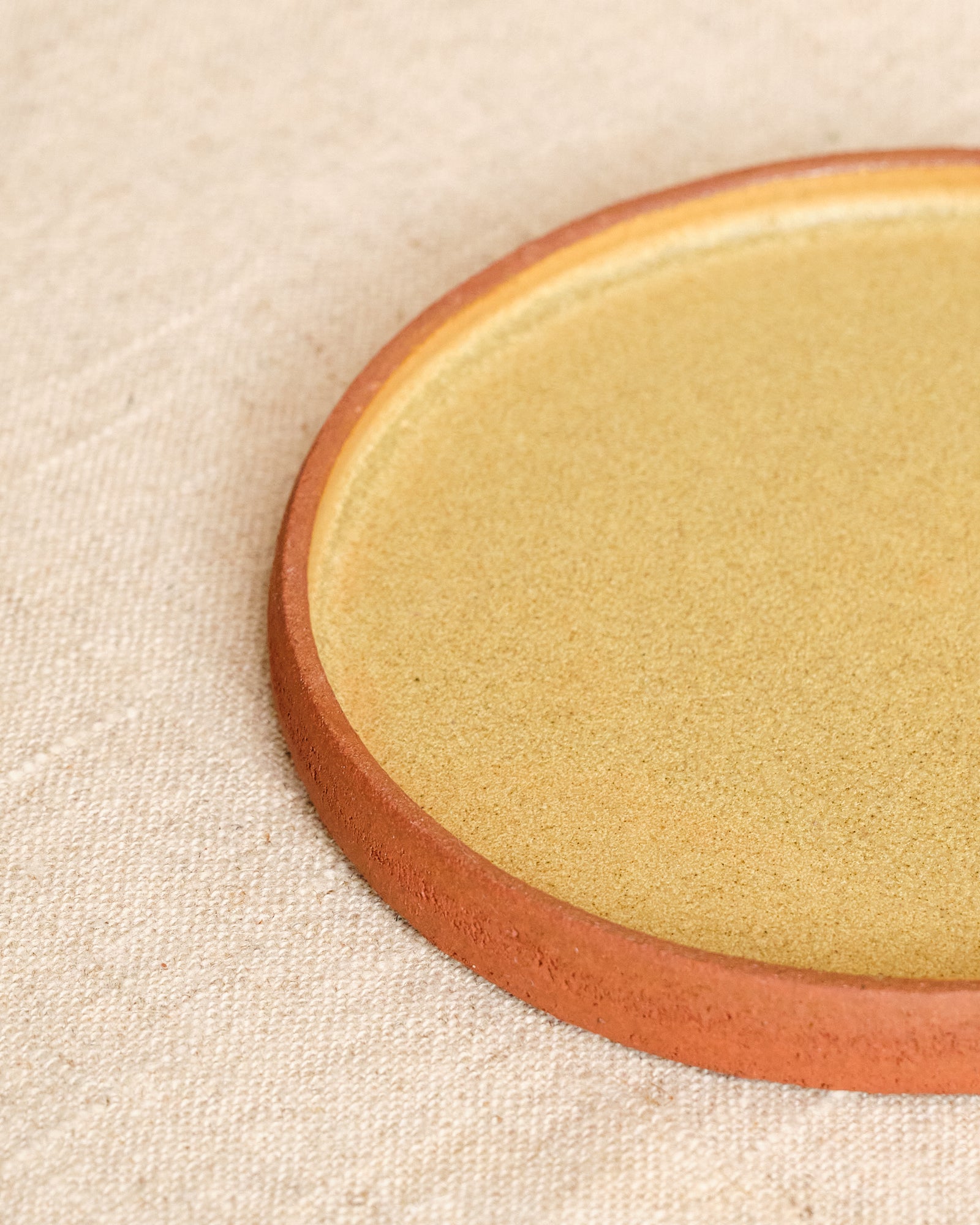 Close-up of a round ceramic plate with a brown rim on a beige fabric background