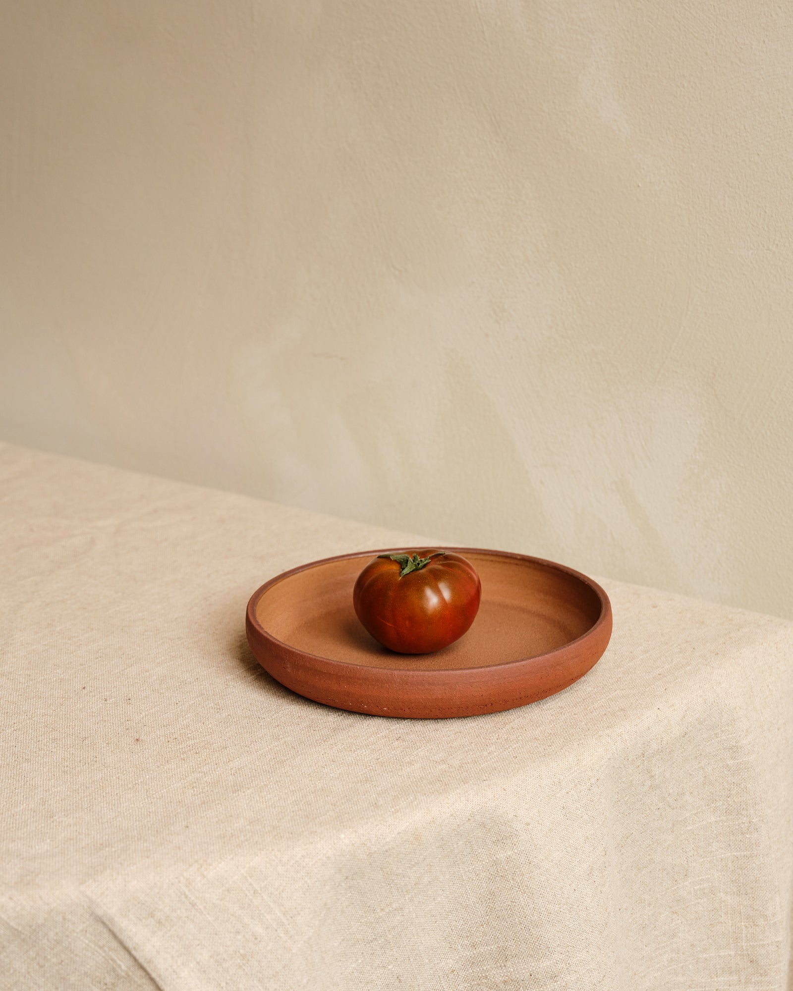 Terracotta plate with a tomato on a beige surface
