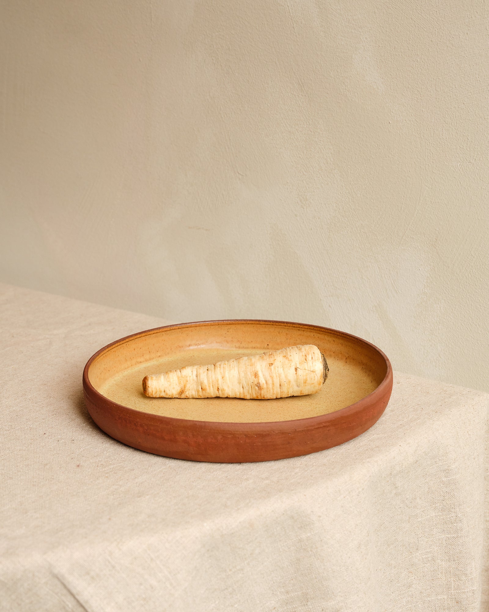 Brown ceramic plate with a single white radish on a beige fabric background