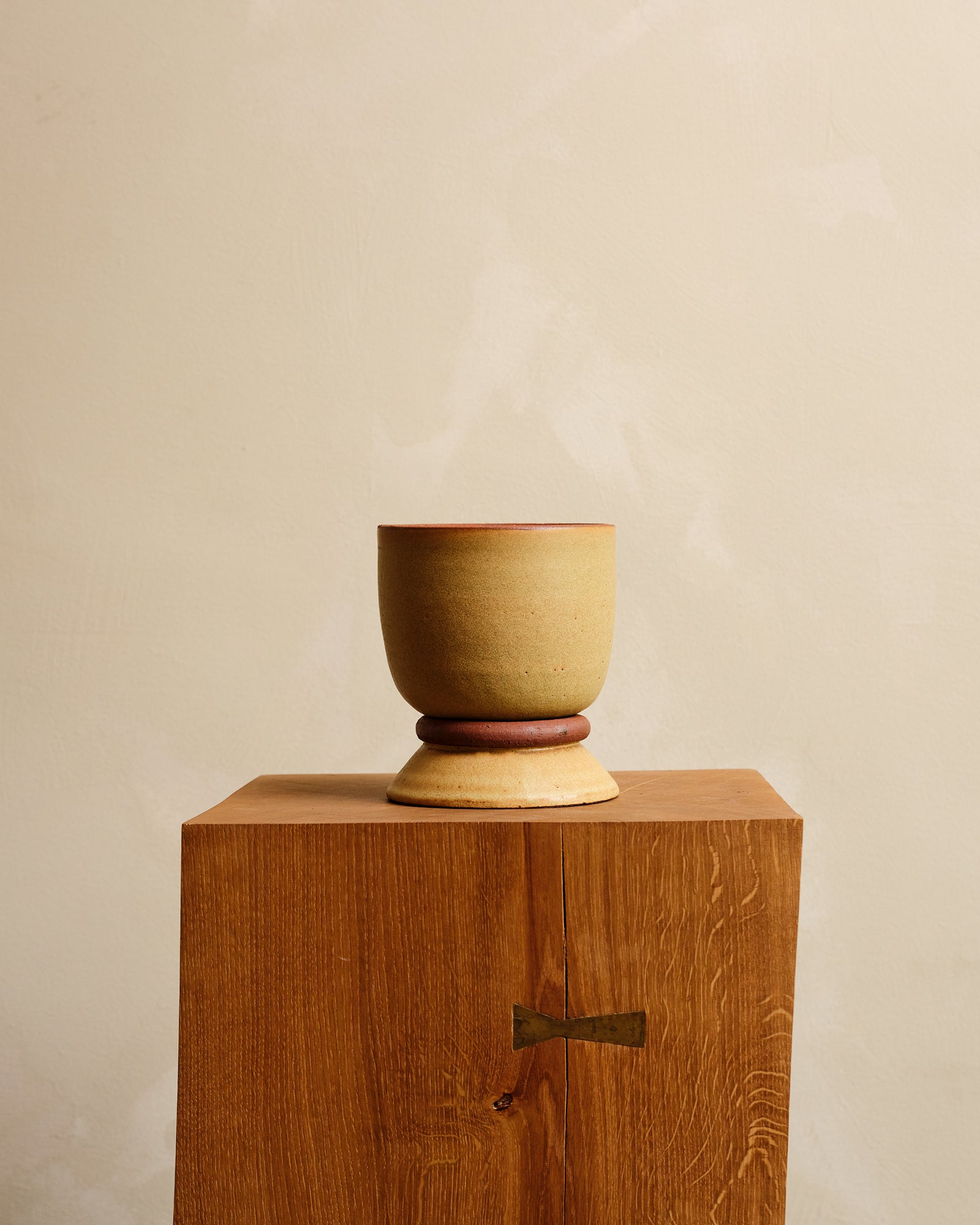 Ceramic planter and saucer on a wooden pedestal against a beige background