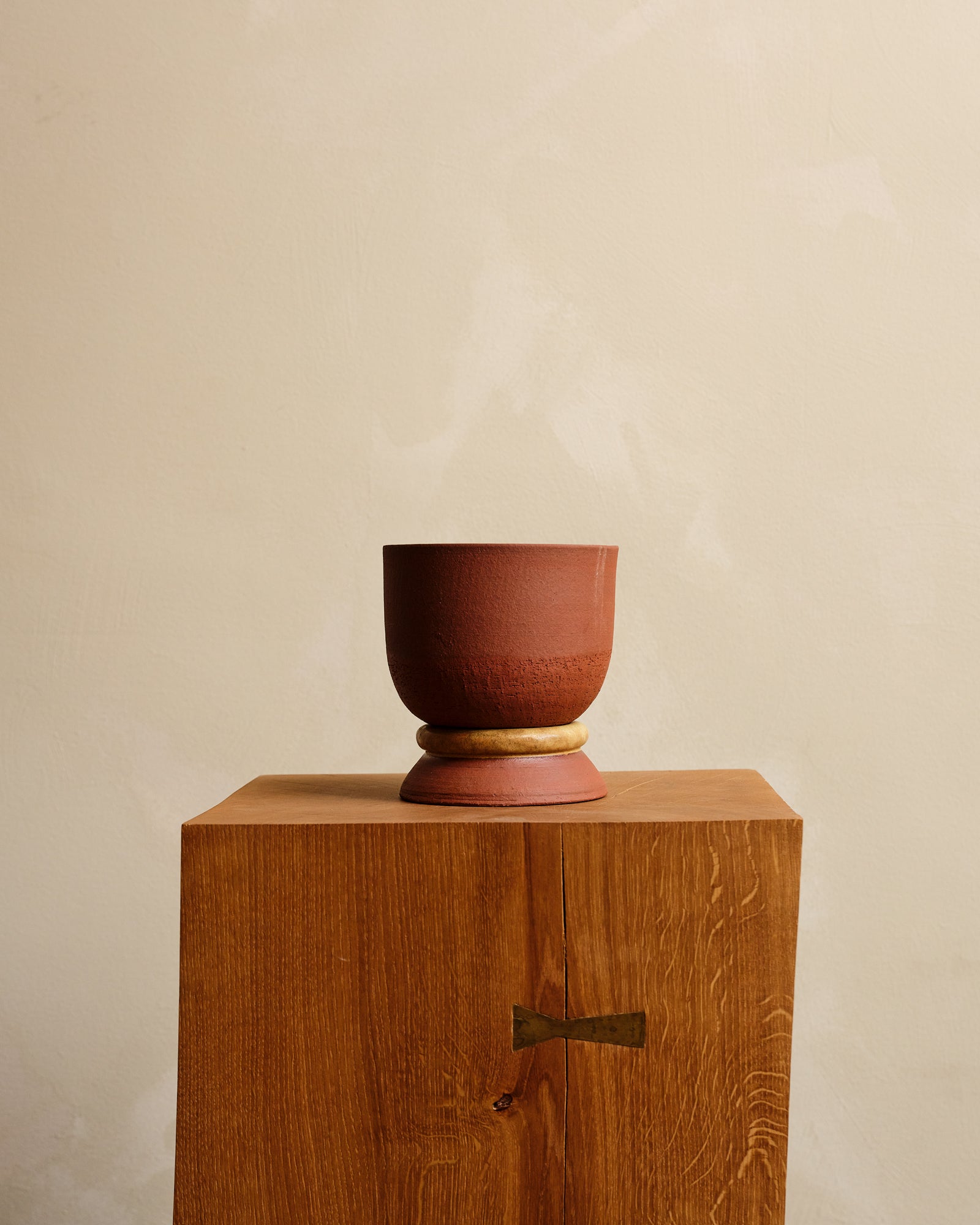 Ceramic planter and saucer on a wooden pedestal against a beige background