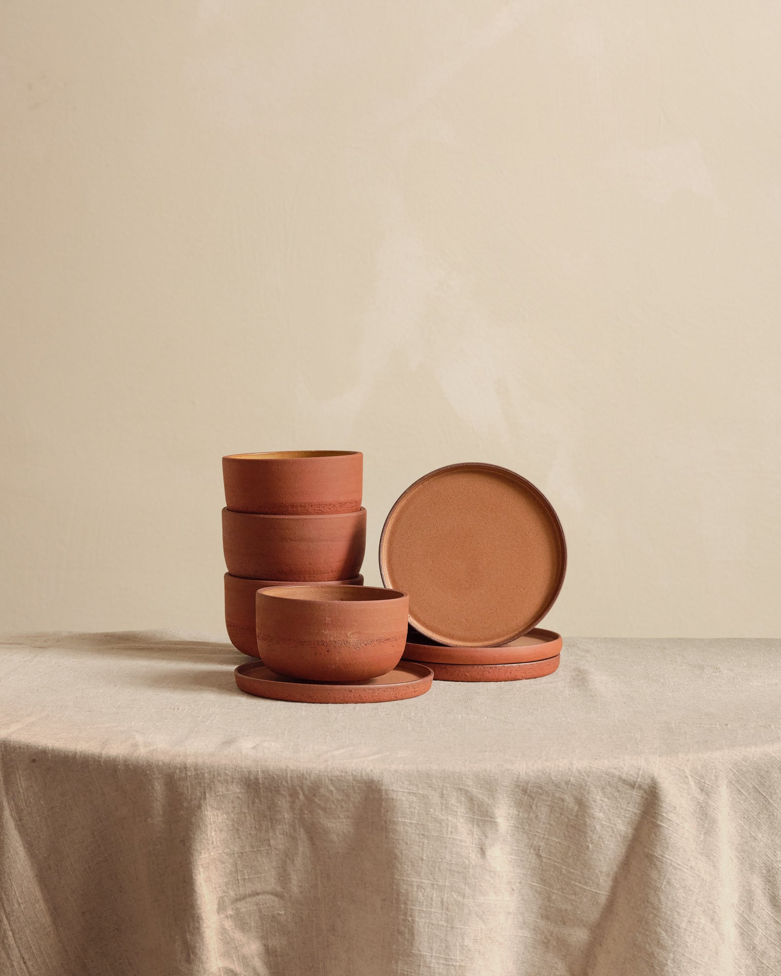 Set of terracotta bowls and plates on a beige tablecloth with a beige background