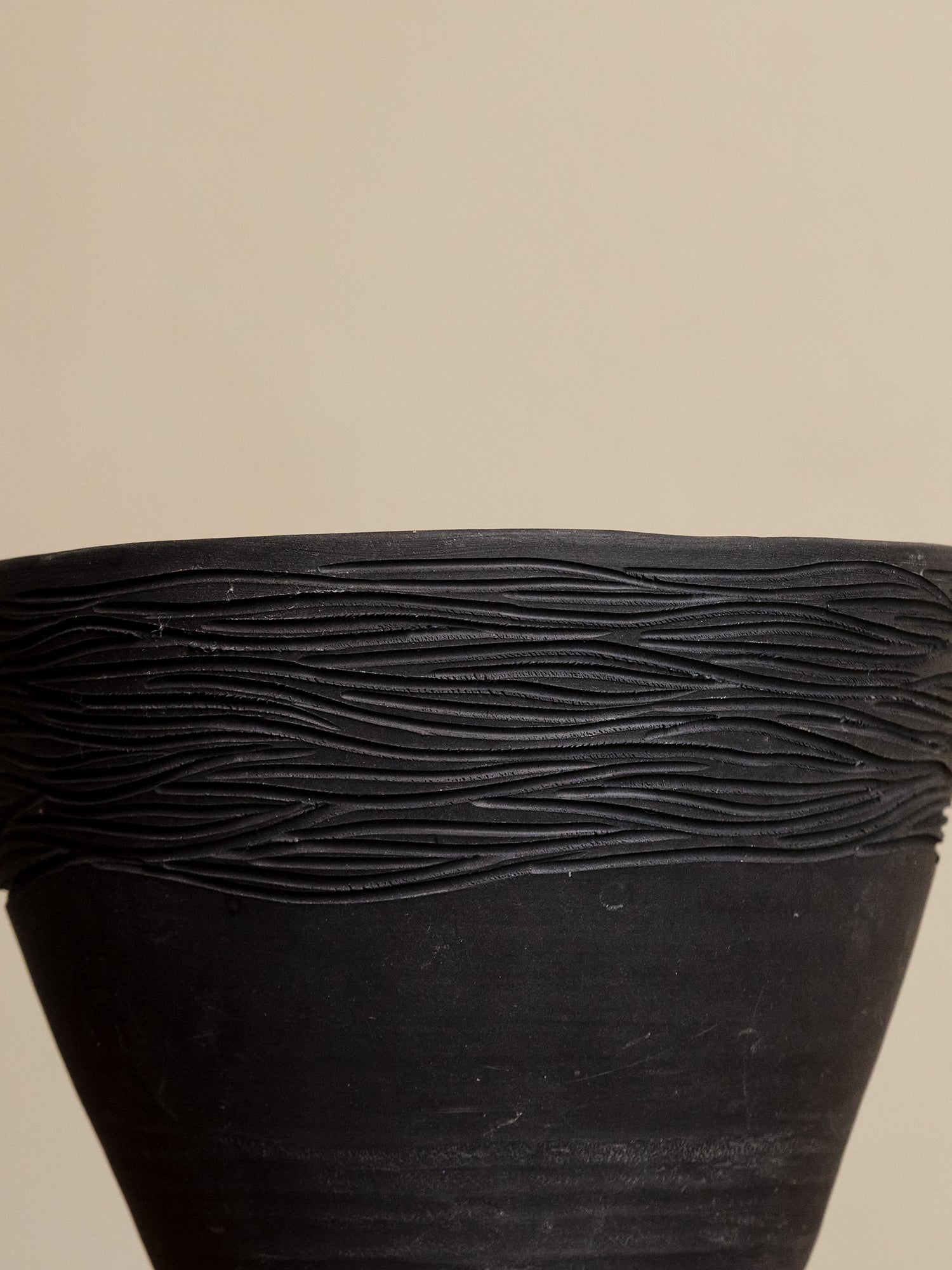 Black textured planter against a beige background