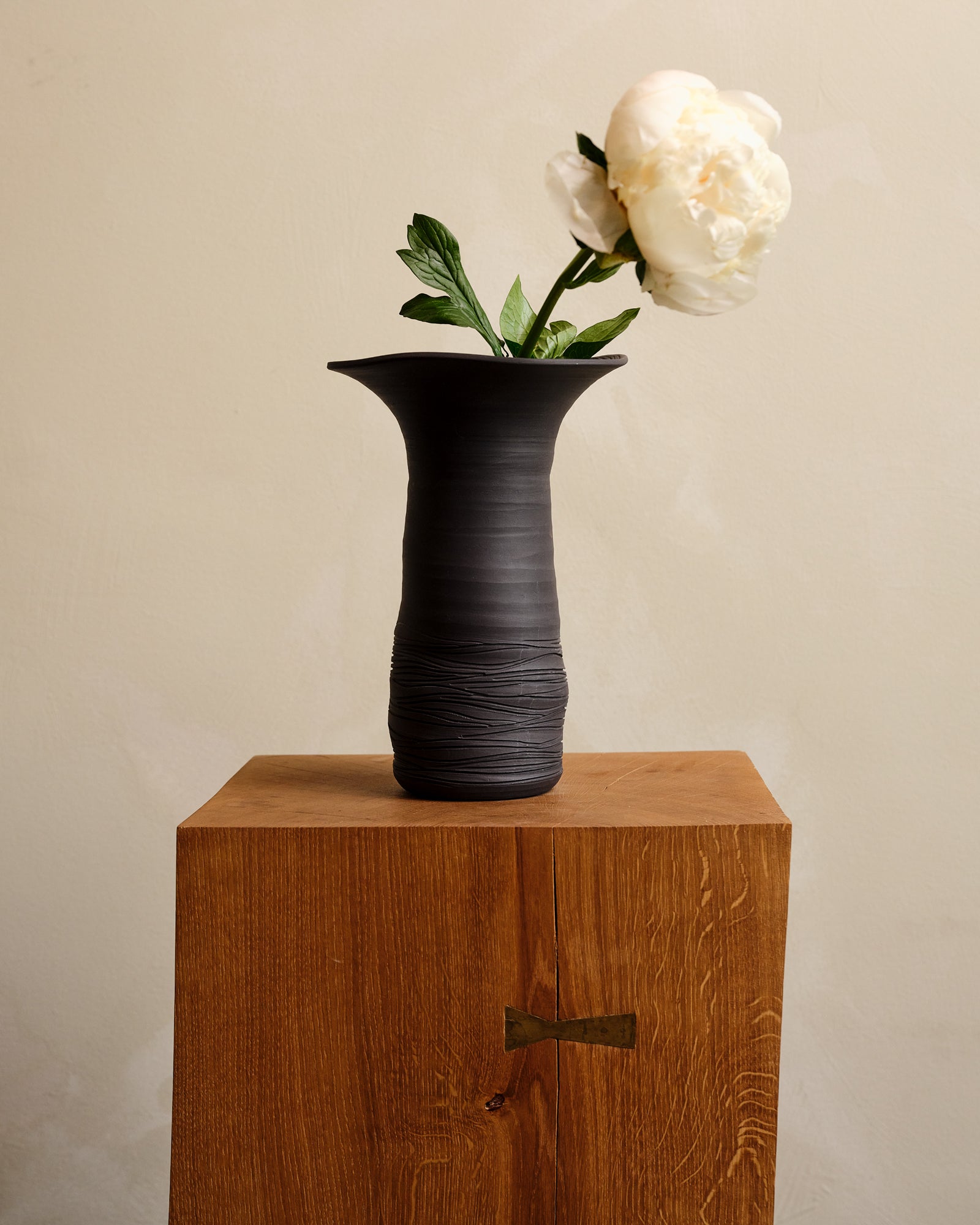 Black vase with a white flower on a wooden surface against a beige wall