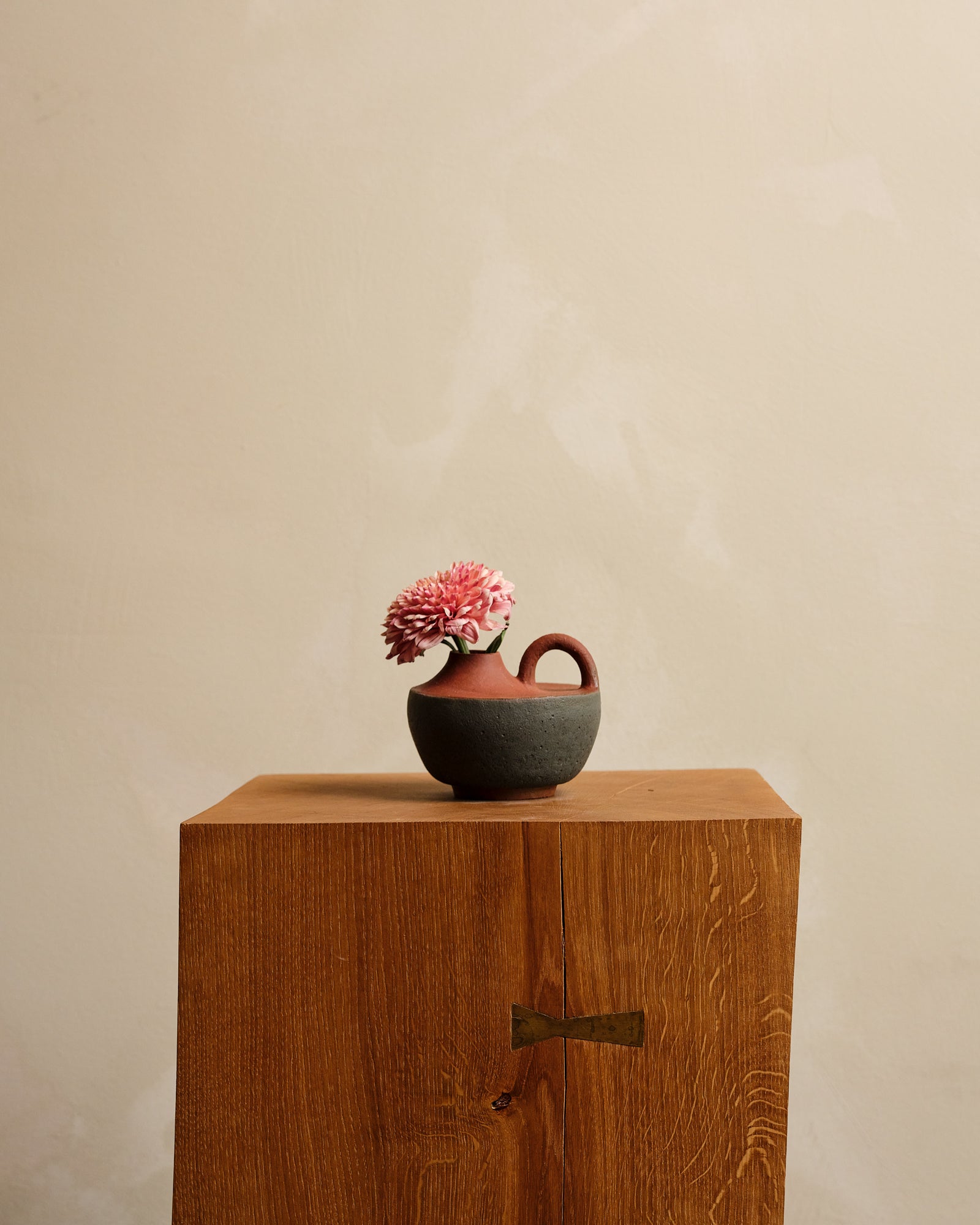 Small ceramic vase with pink flower on a wooden surface against a beige background