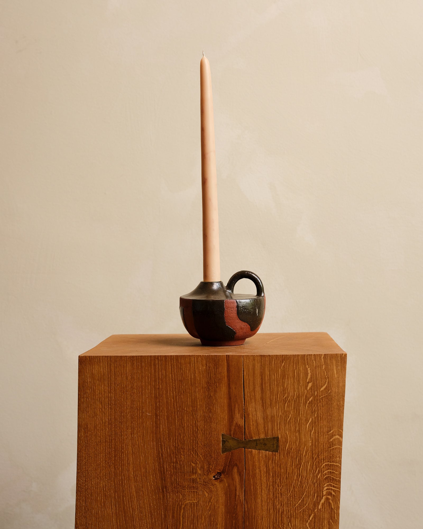 Ceramic vase with candle on a wooden pedestal against a beige background