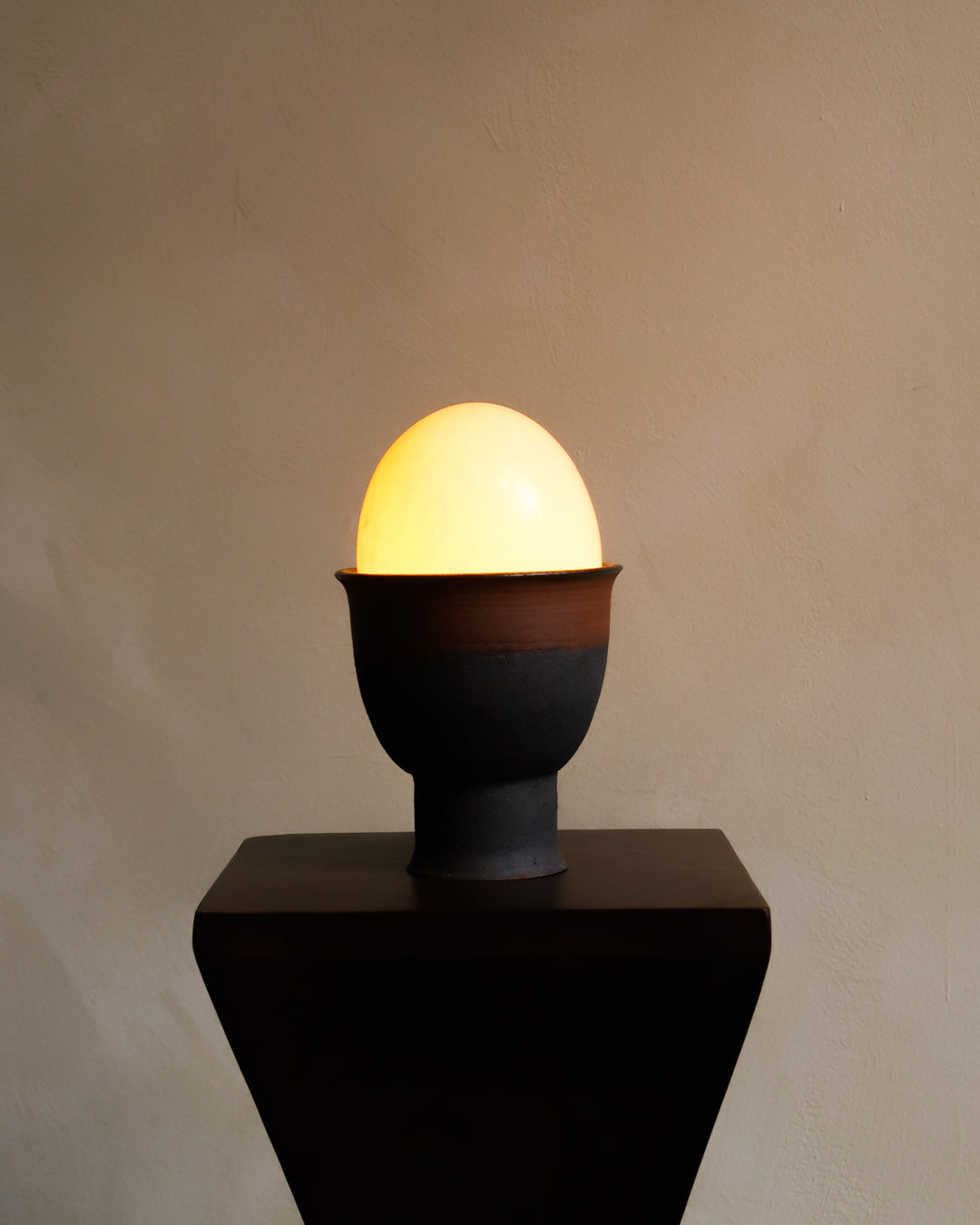 Ceramic egg-shaped lamp with a glowing interior on a plain background