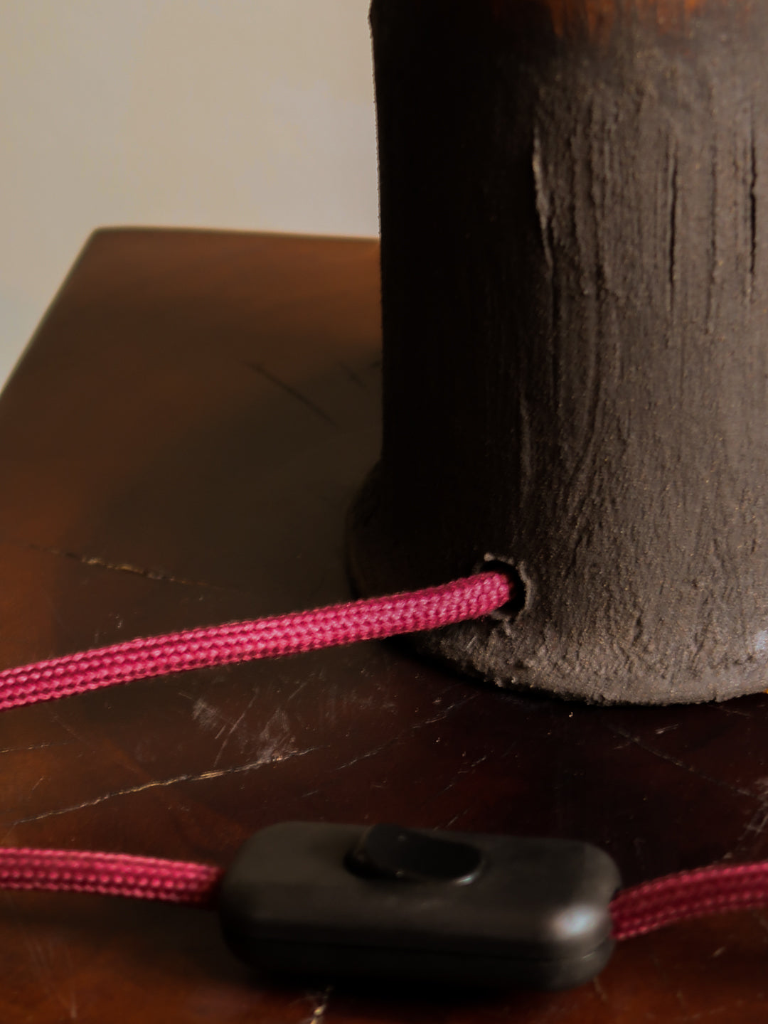 Close-up of a brown textured object with a pink cord and black button on a wooden surface.